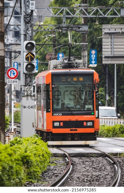 Tokyo, Japan - May, 2022: Orange Tokyo Sakura Tram\
(Toden Arakawa Line) or street car making turn along curved track\
in rainy season
