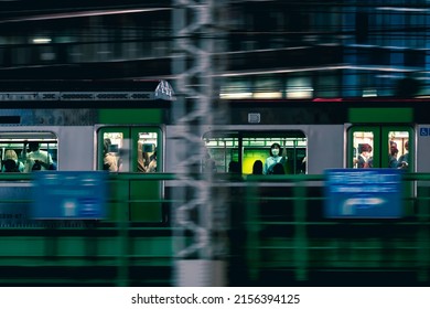 Tokyo, Japan - May, 2022: Pan Shot Of JR Yamanote Line Train Crammed With Crowd Of Commuter Speeding Through Commercial District Of Shinjuku City During Night Rush Hour