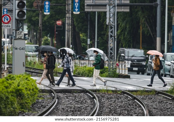 Tokyo, Japan - May, 2022: Pedestrian walking in\
rain across the track of Tokyo Sakura Tram (Toden Arakawa Line)\
track at level crossing