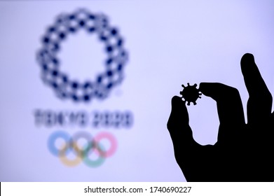 TOKYO, JAPAN - MAY 25, 2020: Hands Silhouette Holds Covid 19 Virus, Summer Olympic Game Tokyo 2020 In Background