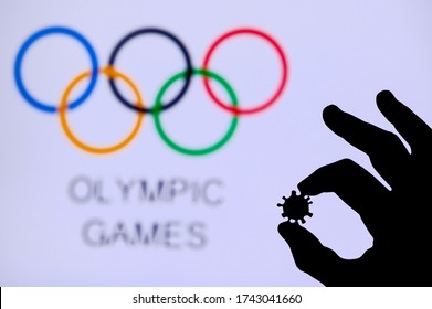 TOKYO, JAPAN - MAY 25, 2020: Hands Silhouette Holds Covid 19 Virus, Olympic Circle In Background