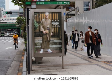 TOKYO, JAPAN - November 8, 2020: Street In Tokyo's Hibiya Area With A Bus Stop And A Bullet Train On A Bridge In The Background. People Wear Face Masks During The Coronavirus Outbreak. 