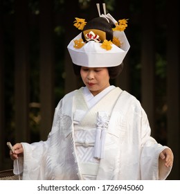 Tokyo, Japan; October 2019: Japanese bride wearing traditional white kimono, hat with yellow ornaments is symbol of obedience and gentleness, holding a fan, wedding at Shinto sanctuary, Tokyo, Japan