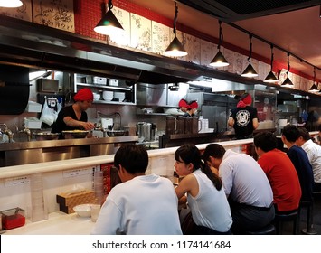 Tokyo, JP - AUGUST 15, 2018: A Lot Of Customers Sitting In Front Of The Desk Bar And Eating Their Dinner In The Japanese Noodle Ramen Restaurant.