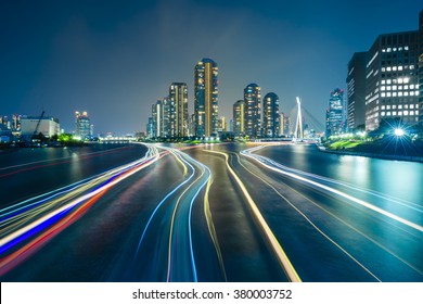 Tokyo skyline by night in modern Tsukishima district with scenic water reflection and boat light trail in Sumida river waters. Soft focus and motion blur due to long exposure shot.