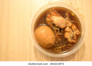 Tom Kai Palo (thai Word) Boiled Egg Stewed And Chicken Meat In Sweet Brown Gravy, In Plastic Bowl Isolated On Wooden Background.