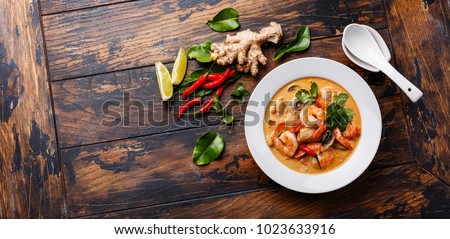 Tom Yam kung Spicy Thai soup with shrimp, seafood, coconut milk and chili pepper in bowl on wooden background copy space