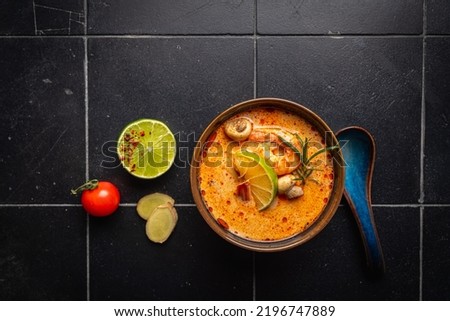 Tom Yam kung Spicy Thai soup with shrimp, seafood, coconut milk and chili pepper in a bowl, top view with copy space