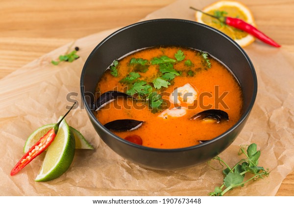 Tom yam soup with shrimp\
and mussels in a bowl on a light wooden background close-up.\
Restaurant food from the chef. Horizontal orientation with a\
copyspace.