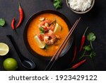 Tom Yum kung Spicy Thai soup with shrimp in a black bowl on a dark background, top view