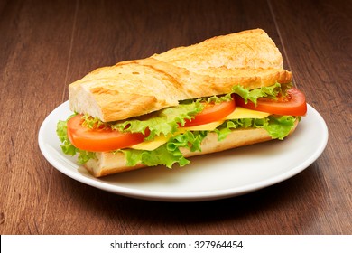 Tomato, Cheese And Salad Sandwich From Fresh Baguette On White Ceramic Plate On Dark Wooden Table Background