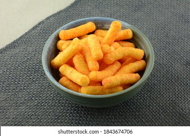 Tomato flavored corn puffs snack in ceramic bowl on grey table runner