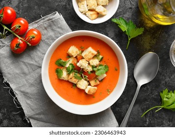 Tomato gazpacho soup with croutons in bowl over dark stone background. Cold summer soup. Top view, flat lay