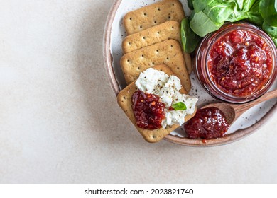 Tomato jam, confiture or sauce in glass jar with crackers and green leaves salad. Unusual savory jam. Mediterranean cuisine. Selective focus. Top view. - Shutterstock ID 2023821740