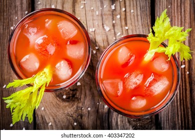 tomato juice with celery and ice in glasses on a wooden table
