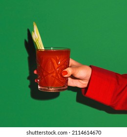 Tomato juice. Female hand holding glass with cocktail bloody mary isolated on green neon background. Concept of taste, alcoholic drinks. Complementary colors, blue, red and green. Copy space for ad