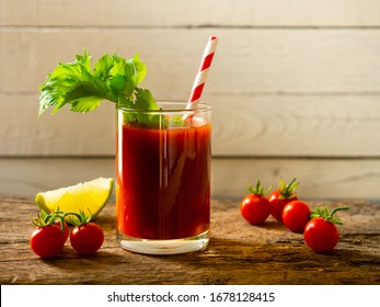 Tomato juice with fresh celery in glass, fresh cherry tomato and lime on a wooden table.