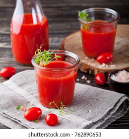 Tomato juice in glass with cress salad, fresh tomatoes on wooden cutting board and grey towel.