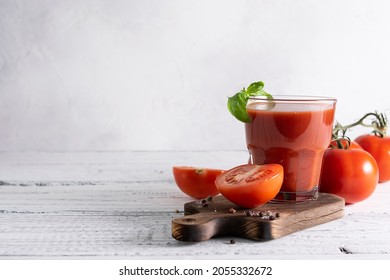 Tomato juice in a glass glass on a dark wooden plate. Halves of tomatoes, peppers and basil in the background. Place for text