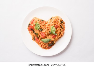 Tomato pasta with basil in a heart shape on white plate, top view, flat lay