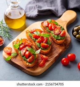 Tomato, Pesto Bruschetta, Crostini With Fresh Basil On Wooden Serving Board. Grey Background. Close Up.