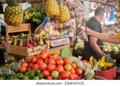 tomato, pineapple, lemon and spices in the foreground with an untrained woman weighing and selling vegetables at a market place - Powered by Shutterstock