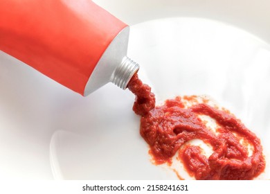 Tomato Puree Or Tomato Paste Spilling Out Of A Tube. On A White Plate.  Selective Focus. 