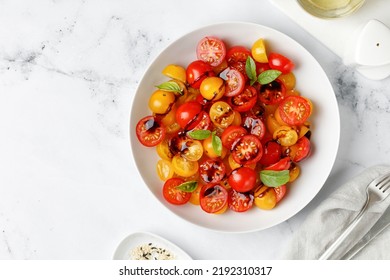 Tomato Salad with cherry red and yellow tomatoes, topping balsamic sauce and basil on white plate and marble background. Keto diet, healthy food. Fresh salad bowl. Top view. - Powered by Shutterstock