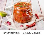 Tomato salsa in a glass jar. Homemade spicy tomato sauce with chilli, garlic and lime. Close up and horizontal orientation. 