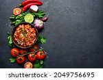 Tomato salsa (salsa roja) - traditional mexican sauce  with ingredients for making on a dark  slate,stone or concrete background.Top view with copy space.