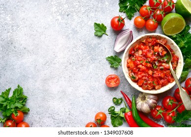 Tomato salsa (salsa roja) - traditional mexican sauce  with ingredients for making on a light grey slate,stone or concrete background.Top view with copy space. 