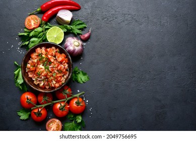 Tomato salsa (salsa roja) - traditional mexican sauce  with ingredients for making on a dark  slate,stone or concrete background.Top view with copy space.