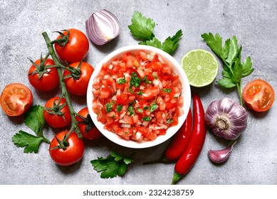 Tomato salsa (salsa roja) - traditional mexican sauce  with ingredients for making on a light grey  slate,stone or concrete background.Top view with copy space.