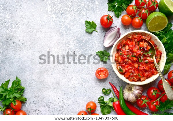 Tomato salsa (salsa roja) -\
traditional mexican sauce  with ingredients for making on a light\
grey slate,stone or concrete background.Top view with copy space.\
