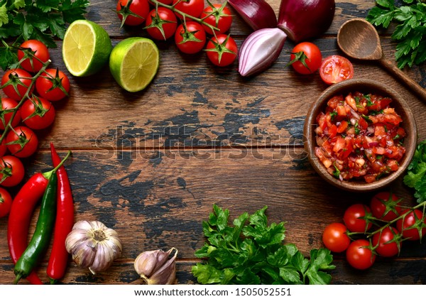 Tomato salsa (salsa roja) - traditional mexican sauce \
with ingredients for making on a wooden background.Top view with\
copy space. 
