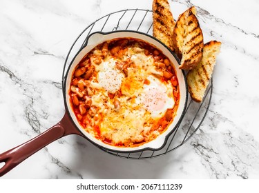 Tomato sauce beans, cheese, eggs baked shakshuka in a ceramic frying pan with a grill crispy bread on a light background, top view                 