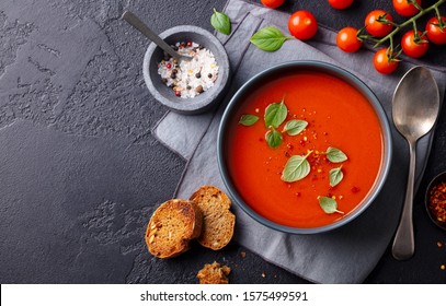 Tomato soup with basil in a bowl. Dark background. Copy space. Top view.