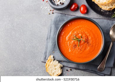Tomato soup in a black bowl on grey stone background. Top view. Copy space.