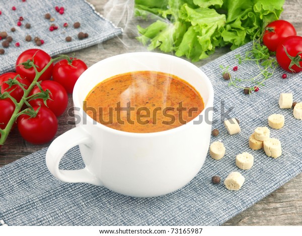Tomato soup with fresh ingredients in a soup\
cup, over an old wooden\
background