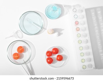 Tomatoes In A Petri Dish On A Laboratory Table. Lab Glassware, Test Tubes And Chemical Substances For Testing Food Quality. Research And Microbiology Inspection, Top View.