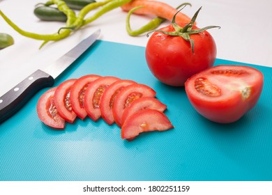 Tomaten, geschnitten mit Messer auf hellblauem Tisch mit Gurken, Pfeffer und Karotten