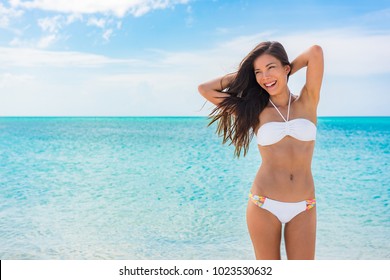 Toned abs sexy slim stomach bikini body woman on beach vacation background for weight loss and fat treatment concept. Happy Asian girl swimsuit model feeling good showing off waist and arms up.