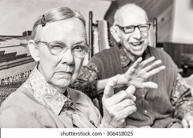 Toned Image Of Angry Old Couple Sitting In Living Room Woman Pointing