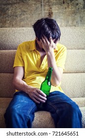 Toned Photo of Sad Young Man with Bottle of the Beer on the Sofa