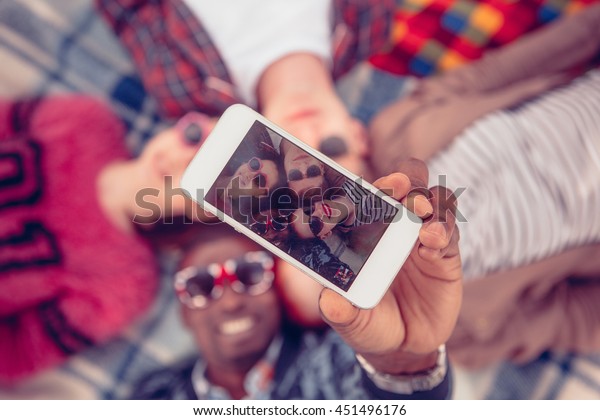 Toned.\
Picture of best friends making selfie on mobile or smart phone\
while spending free time on picnic in\
parkland.