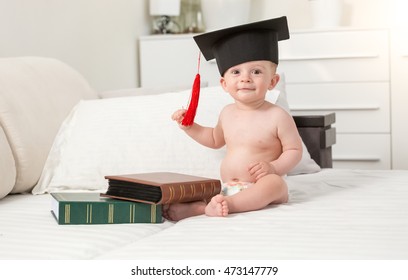 Toned portrait of cheerful baby boy in black graduating cap seating on sofa