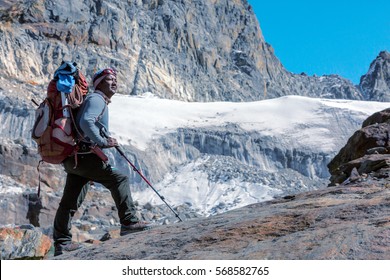 Toned Portrait Of Nepalese Professional Mountain Guide Staying On Rock And Looking Up At High Altitude Summits And Glacier Carrying Backpack With Alpine Climbing Gear