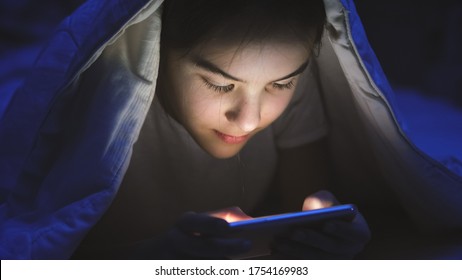 Toned portrait of smiling teenage girl lying in bed with smartphone and browsing internet. - Powered by Shutterstock