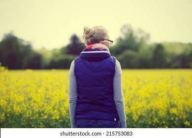 Retrato de una joven hipster con chaqueta violeta y gafas negras paradas en la pradera amarilla
