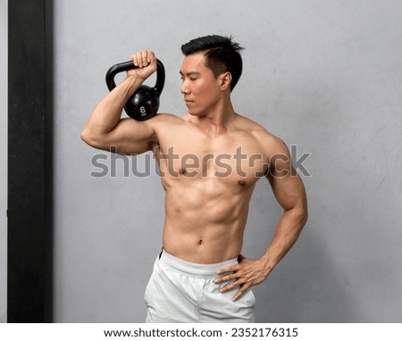 A toned, shirtless Asian man flexes his muscles, the sheen of sweat reflecting his hard work, as he deftly poses with a hefty kettlebell in hand.